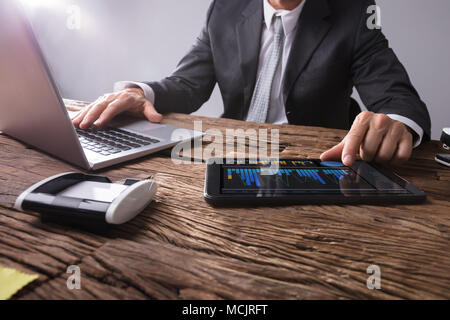 Businessman's Hand Analyzing Graph On Digital Tablet At Workplace Stock Photo