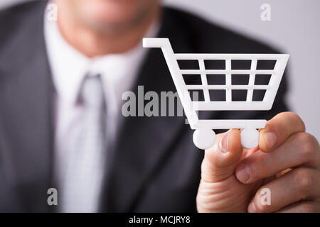 Close-up Of A Businessperson's Hand Holding Small White Shopping Cart Stock Photo
