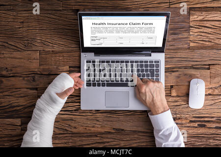 High Angle View Of A Businessperson With Hand Injury Filling Health Insurance Claim Form Stock Photo