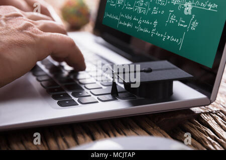 Student Solving Mathematical Problems With Graduation Cap On Laptop Keypad Stock Photo
