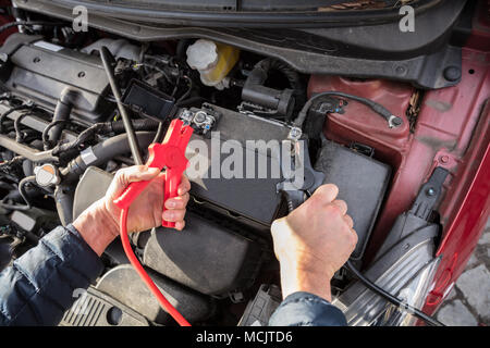 Close-up Of A Person's Hand Using Jumper Cables To Charge Car's Dead Battery Stock Photo