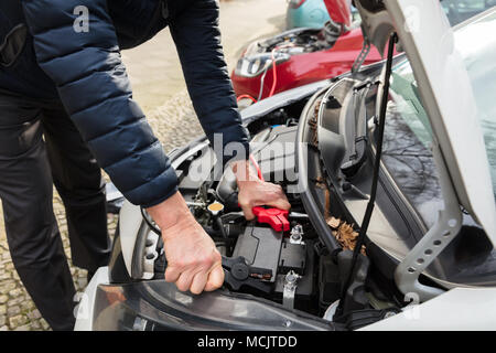 Close-up Of A Person's Hand Using Jumper Cables To Charge Car's Dead Battery Stock Photo