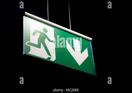 Emergency exit sign hanging on a wall. Emergency exit sign in a building glowing green Stock Photo