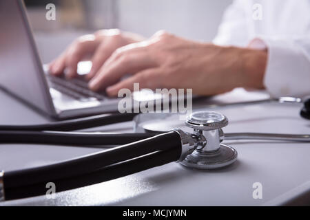 Close-up Of A Stethoscope In Front Of Doctor Working On Laptop Stock Photo