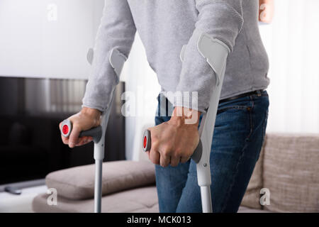 Mid Section View Of A Man With Broken Leg Using Crutches At Home Stock Photo