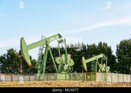 Two active pumpjacks pumping oil out of a well located in the center of France under a blue sky. Stock Photo