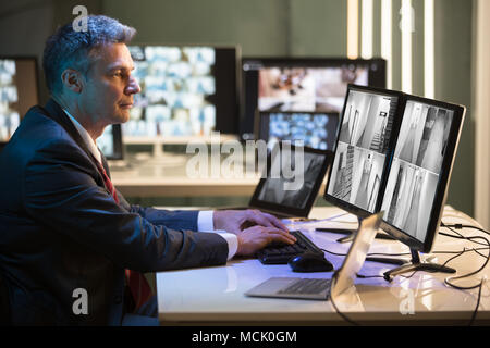 Side View Of A Mature Businessman Looking At CCTV Camera Footage On Multiple Computer Screen Stock Photo