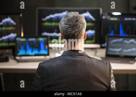 Male Stock Market Broker Looking At Computer And Laptop Showing Graph On Screen Stock Photo