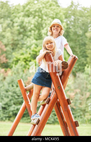 Two sibling children are smiling proudly on the climbing frame in the park Stock Photo