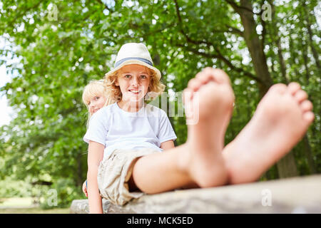 Boy and sister sit relaxed and barefoot in the park in summer Stock Photo