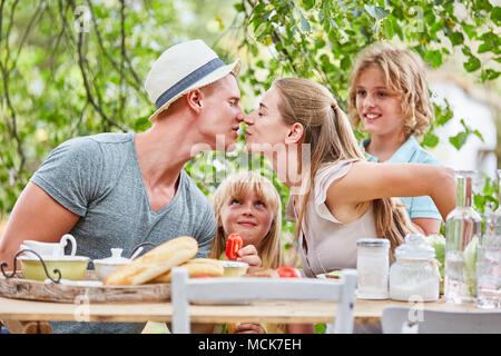 Parents kiss at the breakfast table with children in the garden in the summer Stock Photo