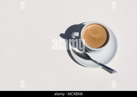 A delicious cup of hot coffee in a white cup and saucer with spoon sitting on a white table overhead view with space on left. Stock Photo