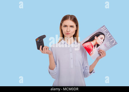 Petite woman making choice between gaming and reading magazine Stock Photo