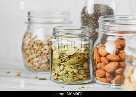 Various nuts and seeds in glass jars over white wooden table against white background. The concept of vegetarian and organic food. Set of photos. Stock Photo