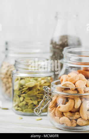 Various nuts and seeds in glass jars over white wooden table against white background. The concept of vegetarian and organic food. Set of photos. Stock Photo
