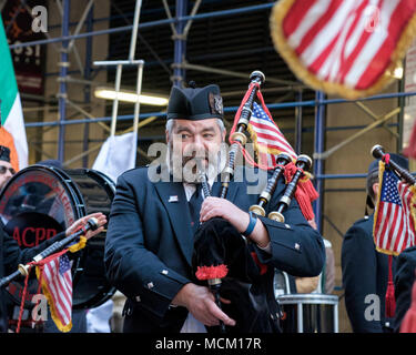 Man from American Celtic Pipe Band blows bag pipes while marching in St. Patrick’s Day Parade, New York City, 2018. Close up.American & Irish flags. Stock Photo