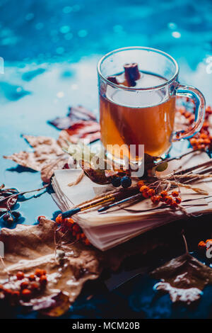 Rainy still life with a glass tea cup on a wet wooden background with copy space. Autumn concept with fallen leaves and a stack of artist scetches Stock Photo