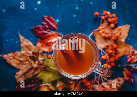 Cinnamon tea flat lay with fallen leaves. Glass tea cup on a wet wooden background with copy space. Autumn still life with herbal beverage. Stock Photo