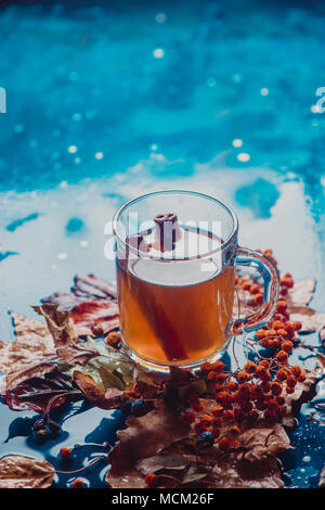 Tea with cinnamon in an autumn still life with fallen leaves and ash berry on a wet wooden background. Seasonal concept with copy space. Stock Photo