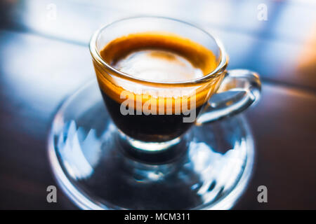 Espresso coffee in glass cup on wooden table, colorful reflections and shallow depth of field. Stock Photo