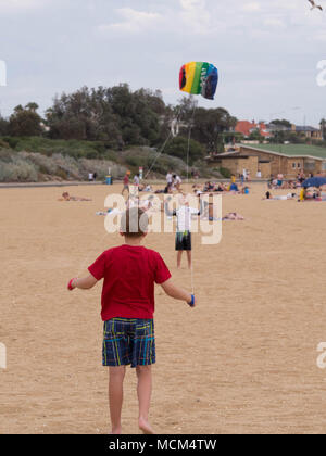 Two little boys one in foreground holding kite controls another in distance holding multicolored kite and launching into the air on beautiful beach. Stock Photo