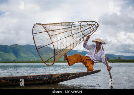 Fisherman wearing traditional clothing balancing in rowboat with fishing basket and paddle, Shan State, Myanmar Stock Photo