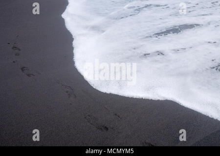 Puerto de la Cruz, Tenerife, Canary Islands; the water's edge as waves break on the black volcanic sand beach. Stock Photo