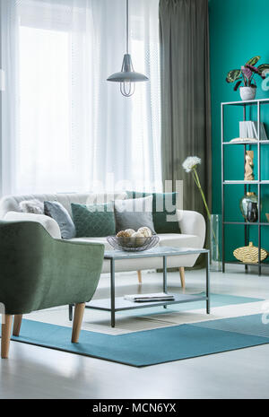 Metal marble table with decorative balls in bowl in green living room interior with light grey sofa and windows with curtains