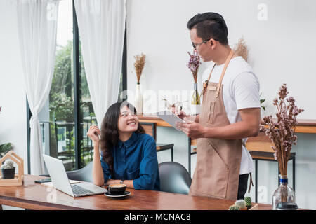 Asia Barista waiter use tablet take order from customer in coffee shop,owner writing drink order at cafe table,Food and drink business concept,Service Stock Photo