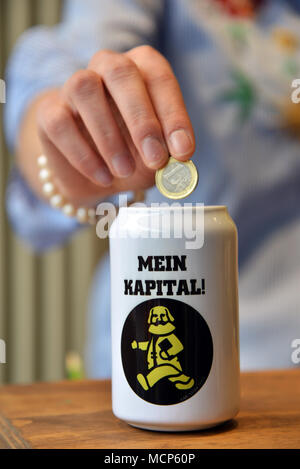 10 April 2018, Trier, Germany: A woman throws a euro coin into a Karl Marx savings box reading 'my capital'. This product and several others have been created on the occasion of the 200th birthday of the philosopher Karl Marx. Photo: Harald Tittel/dpa