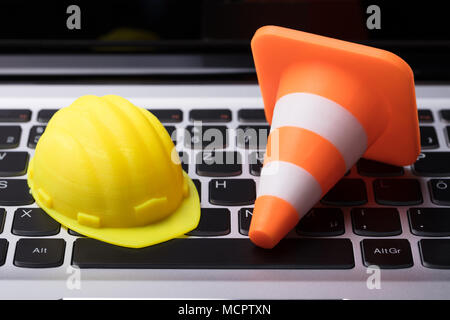 Close-up Of Hard Hat And Traffic Cone On Laptop Keypad Stock Photo