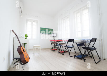 Modern daylight classroom for teaching music. Guitar, white piano and greenboard in modern music classroom Stock Photo