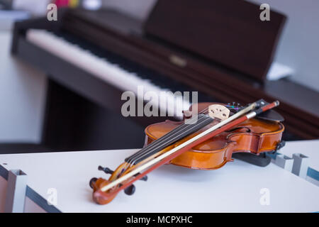 Violin and bow on table with blured dark brown piano in background Stock Photo