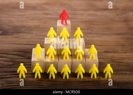 Red Figure Standing On Top Of Yellow Human Figures Over Wooden Blocks Stock Photo