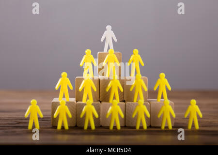 White Figure Standing On Top Of Yellow Human Figures Over Wooden Blocks Stock Photo