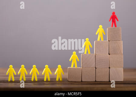 Red Figure Leading Yellow Human Figures On Top Of Wooden Blocks Stock Photo