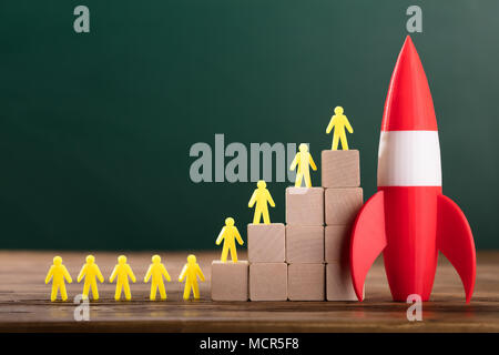 Close-up Of Rocket Besides Yellow Human Figures On Top Of Wooden Blocks In Classroom Stock Photo