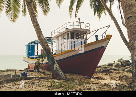 Shipwreck on a Beach. Large fishing boat on the sand on the beach under palm trees on the Indian island. The boat is under repair at the dock. Stock Photo