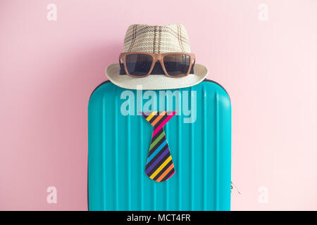 Blue suitcase with hat, sunglasses and paper tie on pastel pink background minimal travel creative concept Stock Photo