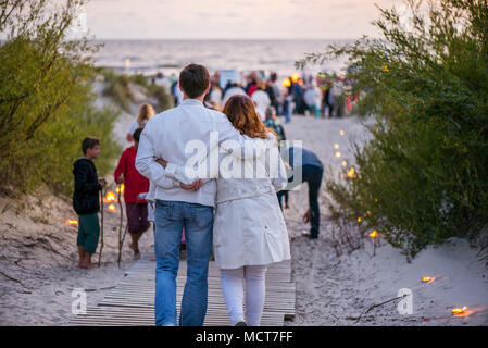 Happy couple hugging and walking on seaside on lit candle path during sunset. Romantic summer evening, love is in the air. People celebrating Night of Stock Photo
