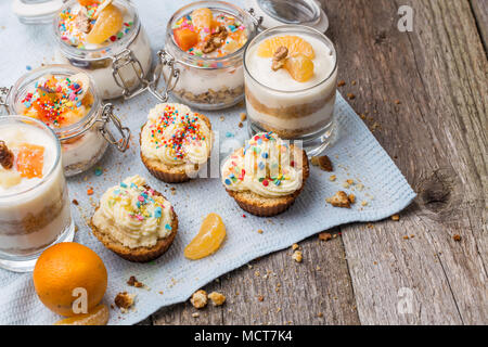 Homemade desserts - biscuits with yogurt, tangerines and walnuts in glass, oats with fresh fruit in glass jar and cupcakes with white frosting and sprinkles. Stock Photo