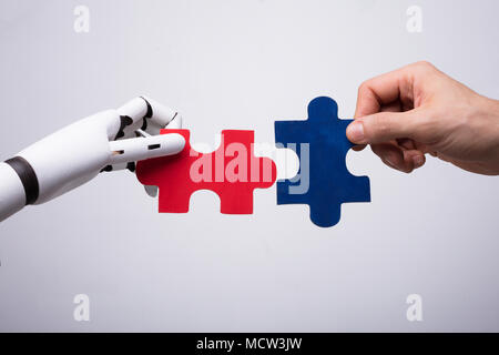 Close-up Of Robot And Human Hand Holding Red And Blue Jigsaw Puzzle Stock Photo