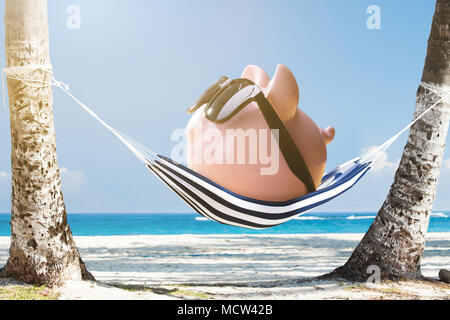 Pink Piggy Bank Wearing Sunglasses Relaxing On Hammock At The Beach Stock Photo