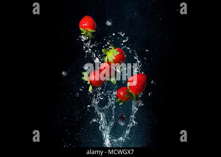 Fresh berries in splashes of water on black background. Juicy strawberries and blueberries. To stop a moment Stock Photo