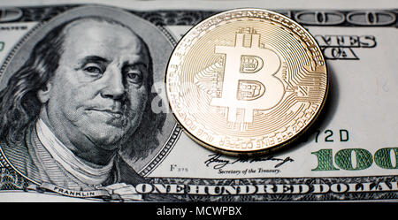 Bitcoin. Gold Bitcoins on a one hundred dollar bill close up Stock Photo