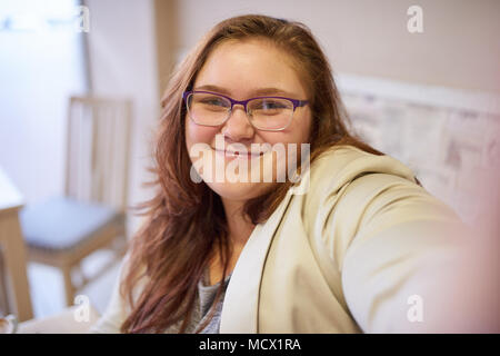 Slightly overweight beautiful young caucasian woman taking a picture of herself while wearing formal clothing and glasses in a cafe to start her day off with a smile and positive energy. Stock Photo