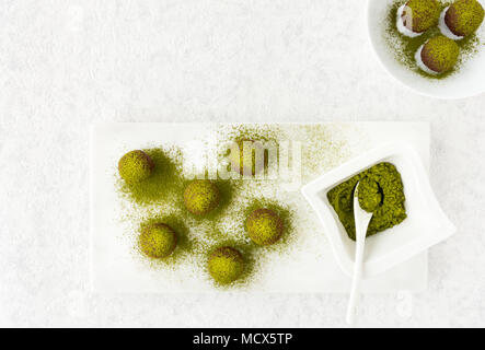 Top view of matcha chocolate truffles and a small bowl filled with green matcha powder on white marble chopping board. Stock Photo
