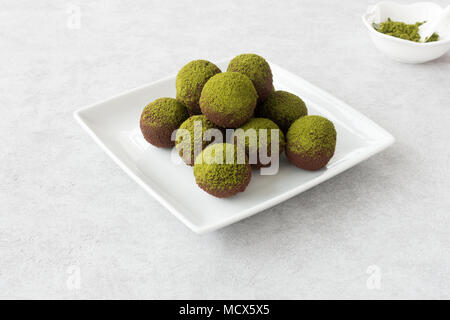 Homemade chocolate truffles dusted with green matcha powder arranged on a white plate. Stock Photo