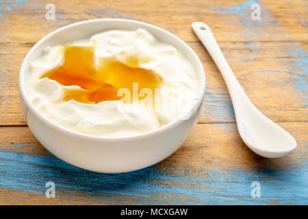 live organic Greek yogurt with natural honey in a white ceramic bowl against grunge wood, top view Stock Photo