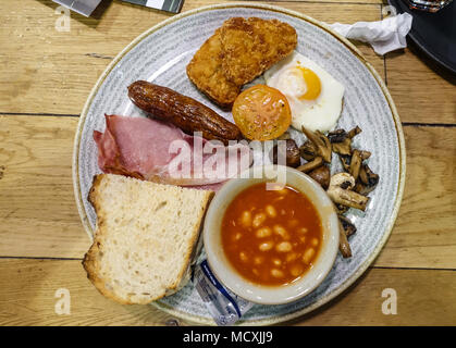A view of a full English breakfast at a cafe with fried egg, sausage, bacon, fried mushrooms, hasb browns and baked beans. Stock Photo